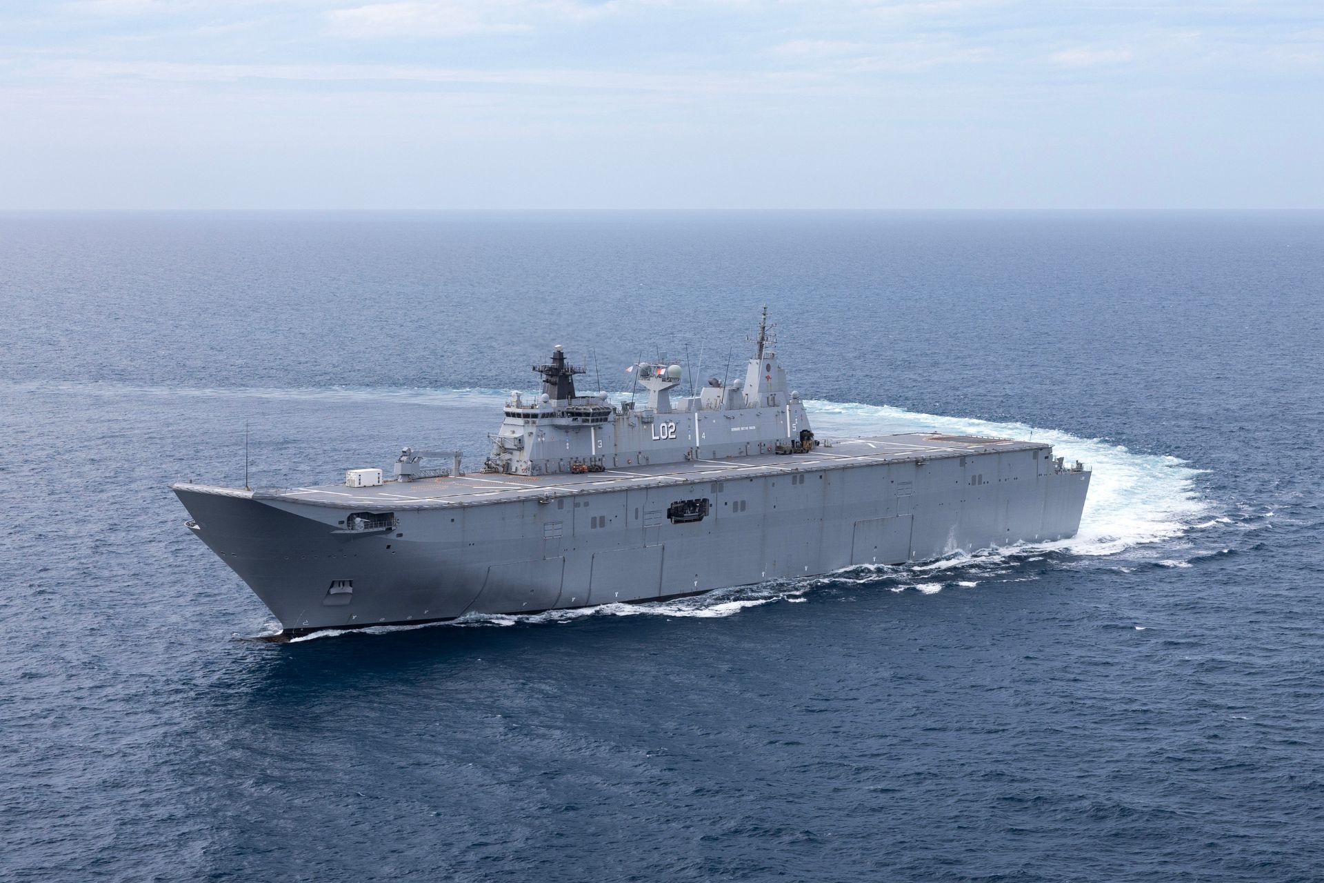 HMAS Canberra transiting offshore, serving as the flagship Landing Helicopter Dock (LHD) at 27,500 tonnes, with a well deck for landing craft and command and control (C2) capability.