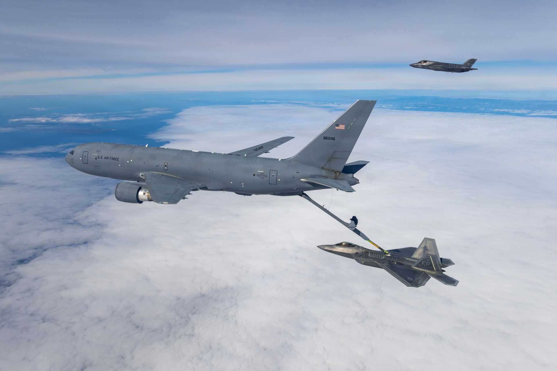 A U.S. Air Force KC-46 Pegasus assigned to the 418th Flight Test Squadron, Global Reach Combined Test Force, conducts aerial refueling operations with an F-22 Raptor from the 411th Flight Test Squadron, Air Dominance Combined Test Force, while an F-35A Lightning II assigned to the 461st Flight Test Squadron, F-35 Integrated Test Force, awaits refueling during integrated flight testing over the Pacific Ocean.