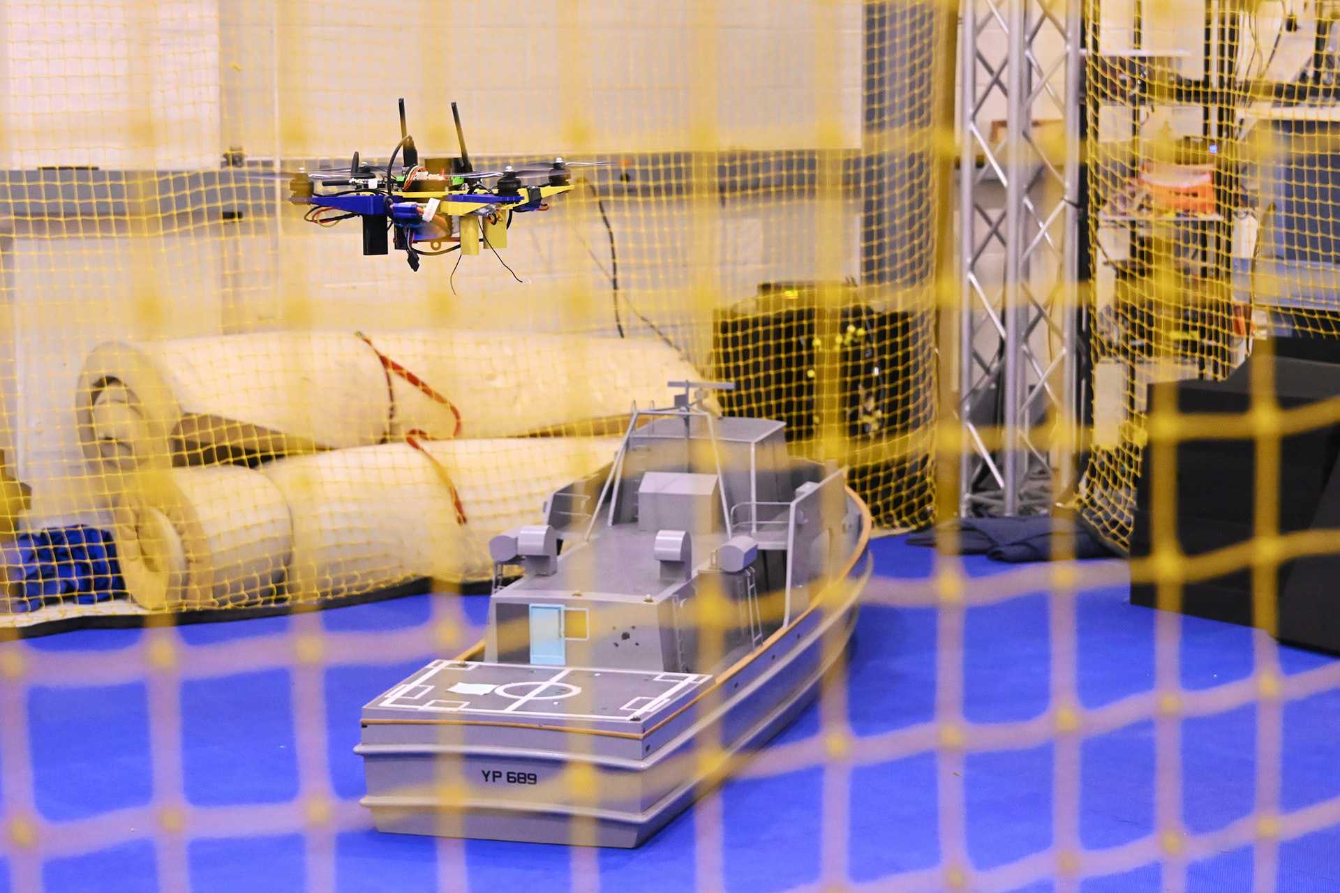 An unmanned aerial vehicle maneuvers above a scale model of a U.S. Navy Yard Patrol craft during indoor testing at the Naval Air Warfare Center Aircraft Division (NAWCAD). The tests evaluate computer-vision navigation and autonomous flight control software designed to enable drones to land on moving warships without GPS or direct pilot control. (U.S. Navy photo by Chuck Regner)