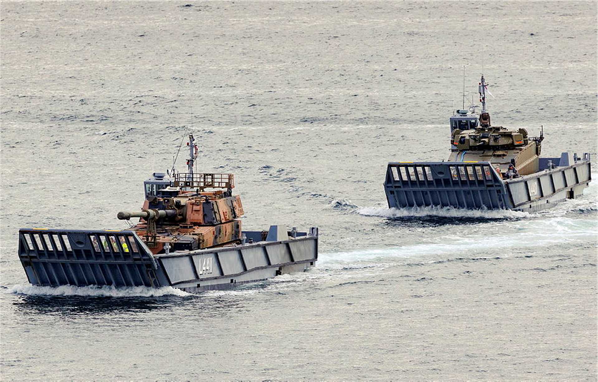An Australian Army AS9 Huntsman 155 mm self-propelled howitzer and AS21 Redback infantry fighting vehicle are transported aboard Royal Australian Navy LCM-1E landing craft during maritime deployment trials at Garden Island in Sydney Harbour, validating their ability to support amphibious and littoral operations in the Indo-Pacific.