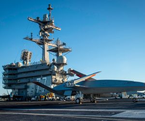 A Boeing unmanned MQ-25 aircraft is given operating directions on the flight deck aboard the aircraft carrier USS George H.W. Bush (Picture source: US DoD)