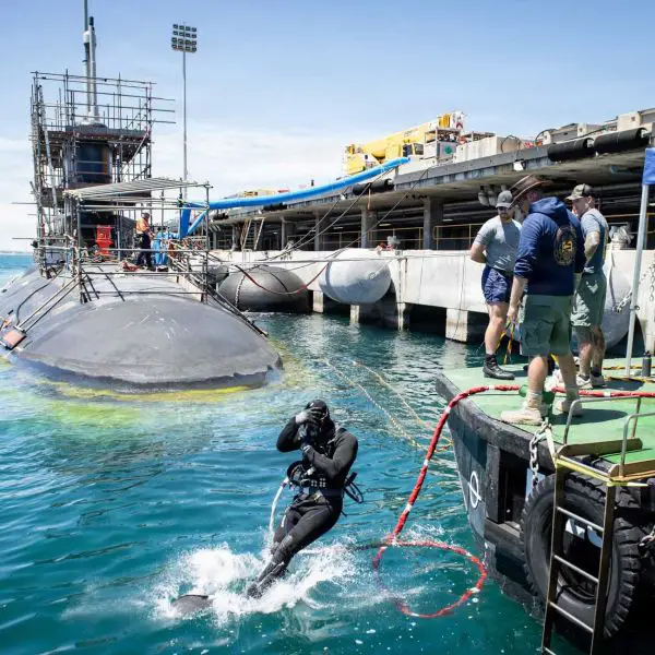 U.S. Navy sailors and Pearl Harbor Naval Shipyard civilian divers work with Royal Australian Navy Clearance Dive Team 4 beneath the hull of USS Vermont (SSN 792) during a planned submarine maintenance period, supporting AUKUS efforts to build Australian capacity for forward Virginia-class submarine sustainment.