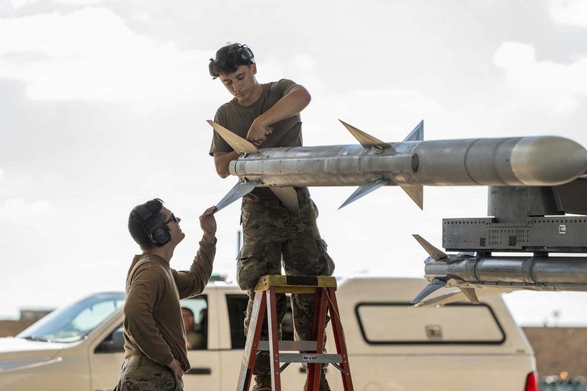 .S. Air Force Tech. Sgt. Jordon Gonzales and Airman 1st Class Lukas Pollock, aircraft armament systems specialists with the Ohio National Guard’s 180th Fighter Wing, prepare the fins of an AIM-120 AMRAAM air-to-air missile mounted on an F-16 Fighting Falcon before a training flight in Swanton, Ohio, on September 29, 2026. (Picture source: U.S. Department of War/Defense)