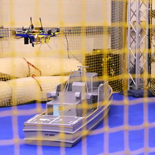 An unmanned aerial vehicle maneuvers above a scale model of a U.S. Navy Yard Patrol craft during indoor testing at the Naval Air Warfare Center Aircraft Division (NAWCAD). The tests evaluate computer-vision navigation and autonomous flight control software designed to enable drones to land on moving warships without GPS or direct pilot control. (U.S. Navy photo by Chuck Regner)