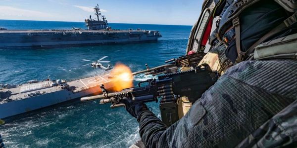U.S. Navy SEALs fire from an MH-60S Seahawk during the Titans of the Sea Presidential Review, conducting live-fire gunnery over an Arleigh Burke-class destroyer as part of a Navy 250 demonstration showcasing integrated special operations and carrier strike group capabilities (Picture source: U.S. Navy).
