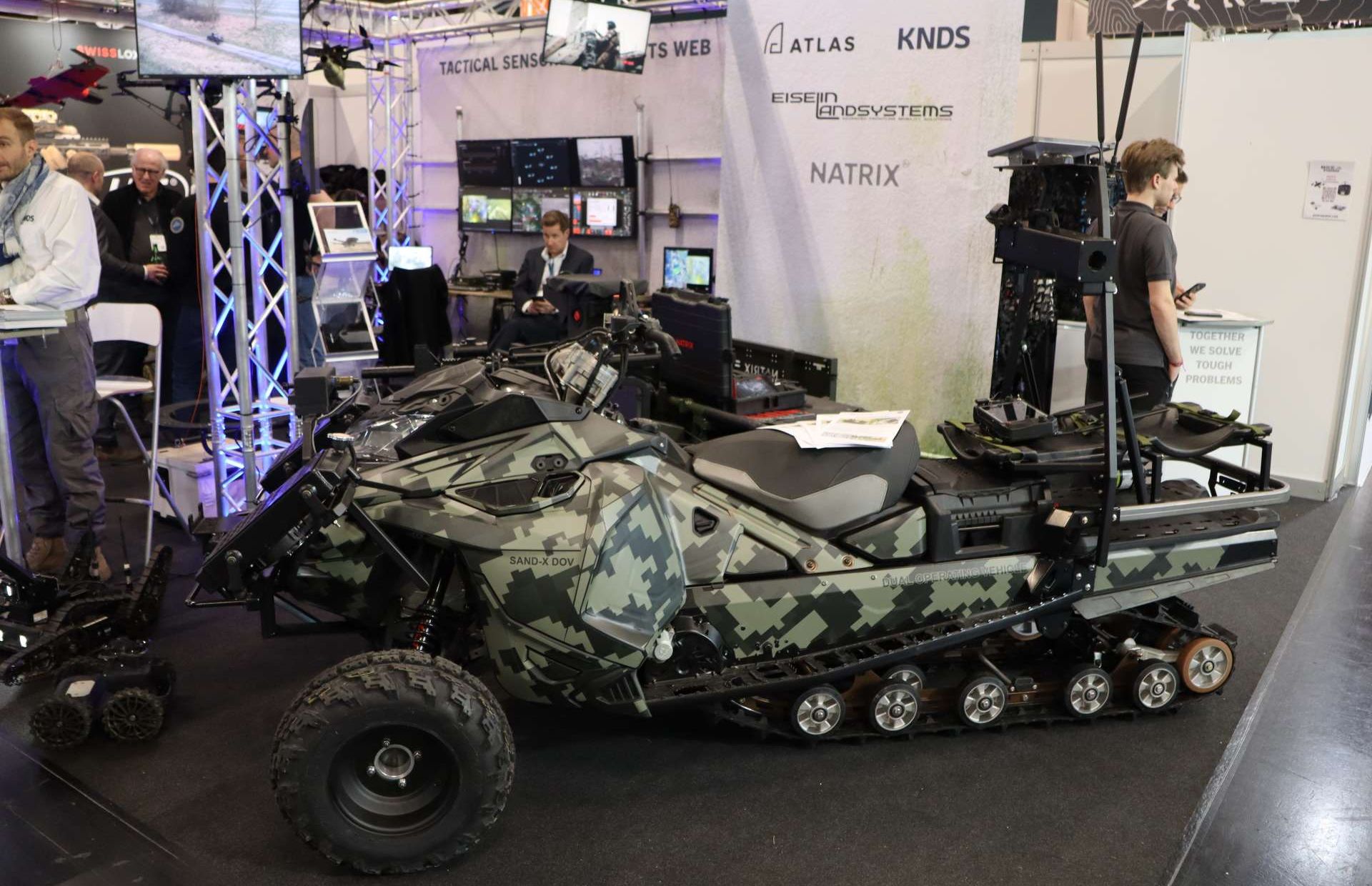 Eiselin Landsystems’ SAND-X Dual Operating Vehicle (DOV) combines high-mobility wheel-and-track performance with “optionally manned” operation, allowing troops to drive it forward and then switch to unmanned mode for last-mile resupply, casualty evacuation, or mission payload delivery in drone- and fire-threatened areas (Picture source: Army Recognition Group).