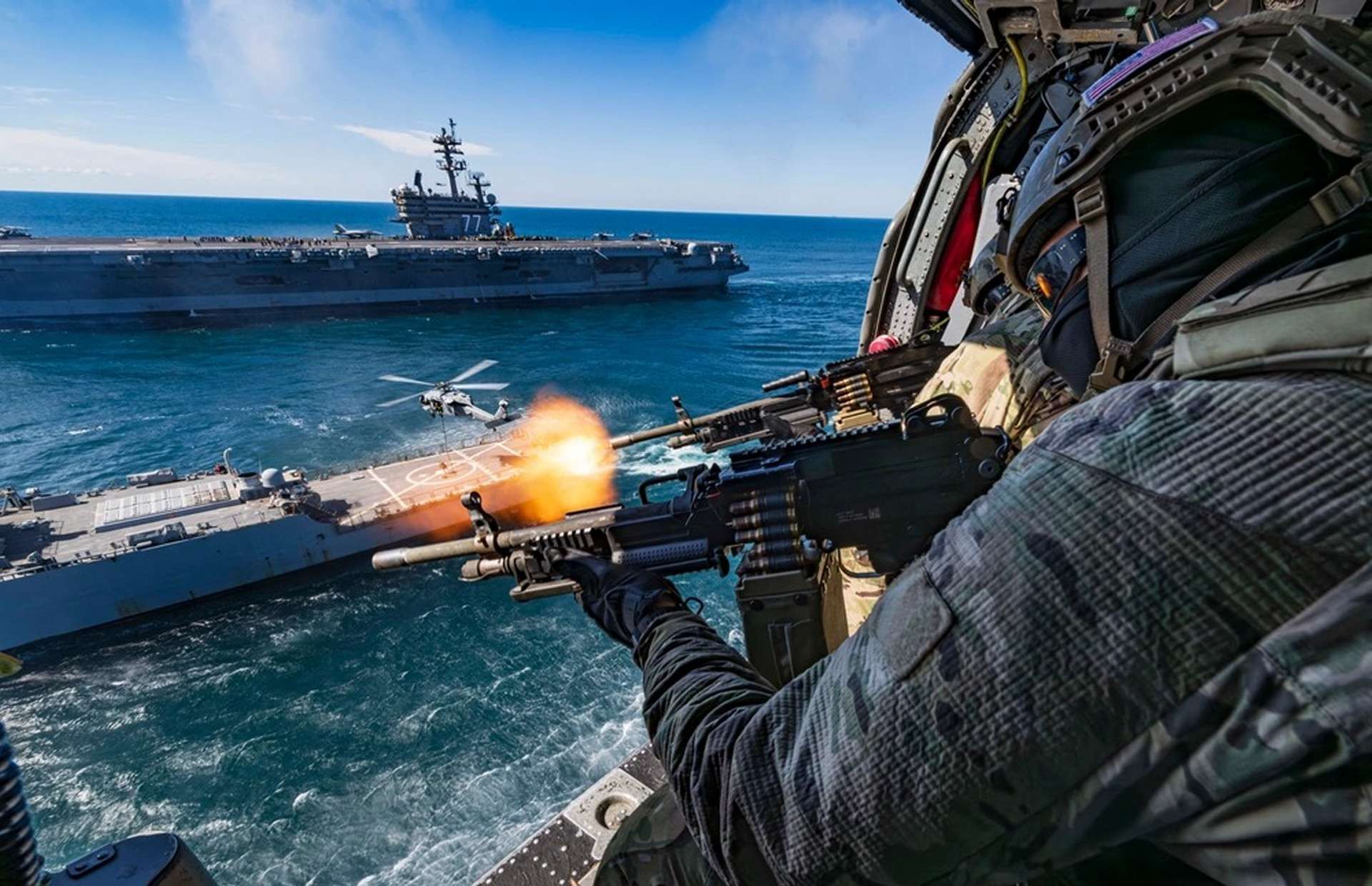 U.S. Navy SEALs fire from an MH-60S Seahawk during the Titans of the Sea Presidential Review, conducting live-fire gunnery over an Arleigh Burke-class destroyer as part of a Navy 250 demonstration showcasing integrated special operations and carrier strike group capabilities (Picture source: U.S. Navy).