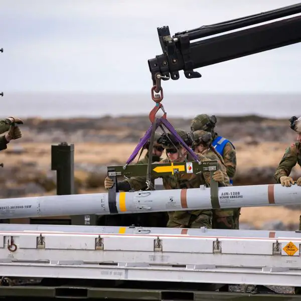 An AIM-120 AMRAAM missile is loaded onto a NASAMS launcher unit during a NATO air defense readiness exercise. The system is designed for rapid engagement of aerial threats including cruise missiles, drones, and aircraft using networked radar and precision-guided interceptors.